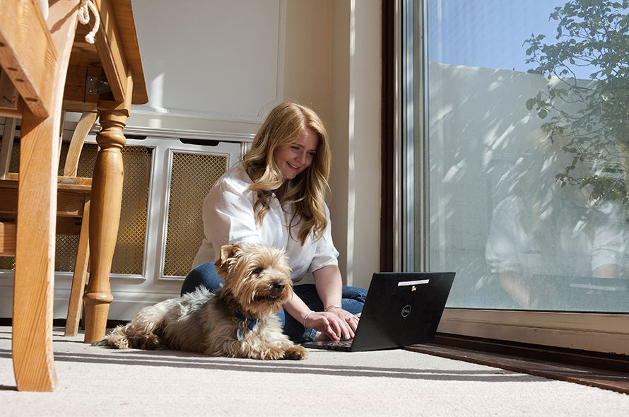 Woman working on computer with dog sitting next to her